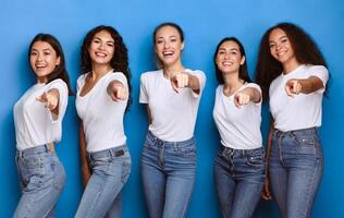 We Choose You. Group Of Multicultural Ladies Pointing Fingers At Camera Standing Posing In Studio On Blue Background. You Are Next Concept. Advertisement Banner photo