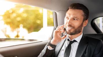 Cheerful CEO or manager talking on mobile phone while going to airport by car, looking through open window. Happy businessman having business conversation while sitting in car, copy space photo