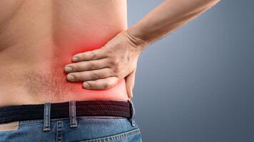 Closeup of unrecognizable topless man touching his loin zone highlighted with red, suffering from chronic or acute kidney disease, grey studio background, copy space. Healthcare concept photo