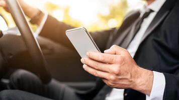 Driving safety concept. Cropped of businessman driving car, using mobile phone, checking location of business meeting, side view, copy space. Unrecognizable man using smartphone while driving photo