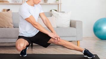 Stretching and workout in morning during covid-19. Muscular guy in sportswear works out at home on mat in interior of living room photo