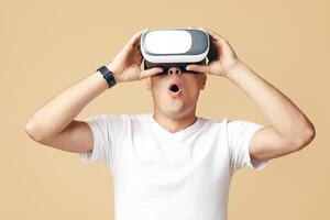 Modern technology, entertainment and virtual world. Surprised zoomer man student with open mouth in white t-shirt with smart watch with vr glasses looking at empty space, isolated on light background photo