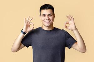 Cheerful contented attractive man enjoys success at work. Handsome young guy with smart watch in casual looks at camera and shows okay gesture isolated on light background, panorama, empty space photo