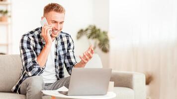 Distance Communication Concept. Portrait of smiling male manager making phone call, sitting on the sofa in living room. Confident adult using computer for work, consulting client online photo