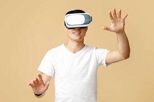 Playing mobile game applications on device. Portrait of young smiling excited student man experiencing virtual reality in vr glasses moves hands controlling gestures, isolated on sand background photo