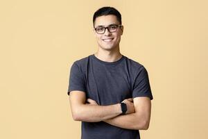 Smiling surprised young man model in casual, glasses and smart watch with crossed arms look at camera, isolated on light background, studio shot photo