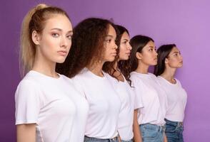 Group Of Serious Multicultural Women Standing In A Row Posing Together Over Purple Background In Studio, Looking At Camera. Female Unity And Diversity Concept. Selective Focus photo