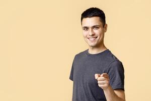 Cheerful man in casual clothes speaks happily at you, chooses to compete, has positive expression. Handsome smart student making choice isolated on light background, empty space, studio shot photo