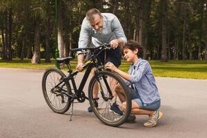 Full length portrait of smiling man and boy repairing bicycle using clippers in nature photo