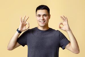 Great choice, big offer, good job and fine blogger review. Handsome cheerful young man student with smart watch showing hands gesture ok, isolated on beige background, studio shot, free space photo