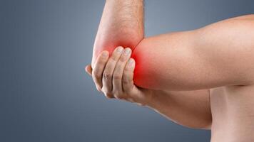 Cropped of topless man having pain in his elbow, touching his injured hand highlighted with red, side view, copy space. Closeup of unrecognizable guy rubbing sore elbow, grey studio background photo