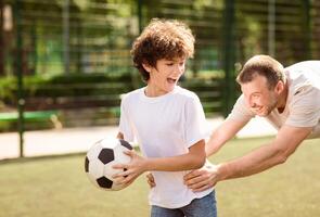 Having Fun. Playful family enjoying football together, laughing kid running from father holding ball photo