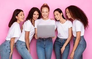 Group Of Multiracial Women Using Laptop Computer Standing Over Pink Background. Internet Browsing, Web Study, Online Education, Services And Technologies Concept. Studio Shot photo