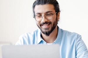 Recruitment Concept. Smiling Eastern Guy Using Laptop, Searching Job Online, Browsing Websites In Internet, Looking For Work Opportunities, Positive Arab Man Sitting At Desk At Home, Copy Space photo