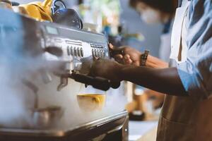 Barista make coffee with espresso machine in cafe and social distancing. Focus on african american man in apron works with equipment, doing drink for client during coronavirus outbreak, cropped photo