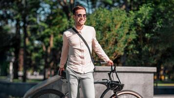 Portrait of smiling handsome hipster businessman in sunglasses with bicycle standing on park background, in autumn photo