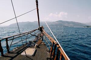 Bow of a wooden sailboat sailing on the sea towards a mountain range photo