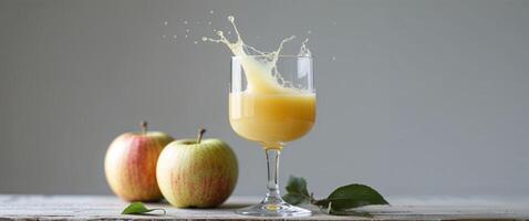A glass of apple juice with a splash surrounded by two apples on a wooden surface and gray background. photo