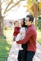 Dad hugging mom from behind with a little girl in her arms in the park photo