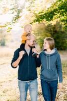 Mom and dad with a little son on his shoulders walk in the park and look at each other photo