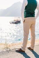 Man with his hands in his pants pockets stands over the sea. Back view. Cropped photo