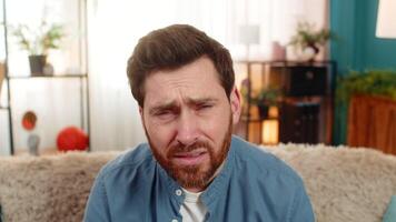 Young man sitting on the sofa at home, squinting at the screen with suspicion, doubting what he sees video