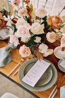 Bouquet of flowers stands on the festive table next to a plate with a menu photo