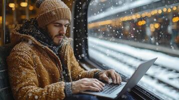 A man in a winter coat and hat sitting on a train using a laptop photo