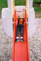 Little girl slides down a slide holding on to the handrails photo