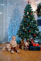 Little girl with a teddy bear sits on the floor next to gifts under the Christmas tree photo