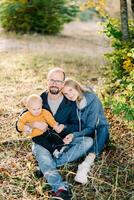 Mom rested her head on the shoulder of dad sitting with his little son on his knees on dry grass photo