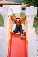 Little girl sits on a slide at the playground holding her hands on the railings photo