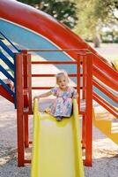 Little girl sits on top of a slide on the playground holding on to the railings photo