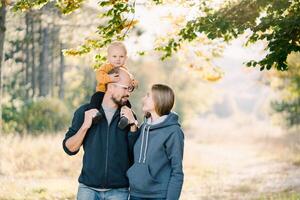 Smiling dad with a little boy on his shoulders stands next to mom and looks at her photo