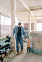 Father and a little girl are walking along the farm near a large bale of hay to the goat pens photo