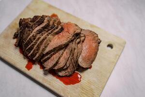 Roast beef slices with blood lie on a wooden cutting board on the table. Top view photo