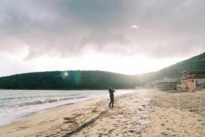 Young man with a colorful kite soaring in the sky walks along a sandy beach. Back view photo