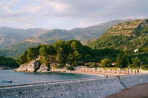 View from the stone isthmus to the sandy beach at the foot of the green mountain range photo