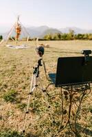 Laptop with a webcam and a microphone on a stand stands in front of a wedding arch on a green meadow photo