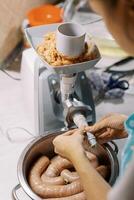 Cook pulls the gut on the electric meat grinder for preparing sausage photo