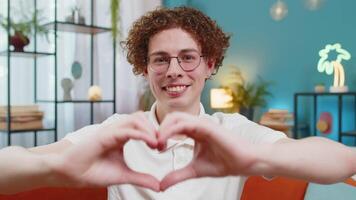 Smiling man at home makes symbol of love showing heart sign to camera express romantic feelings video