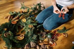 Decorator holds in his hands a sprig of red berries for a Christmas wreath lying on the floor. Cropped photo