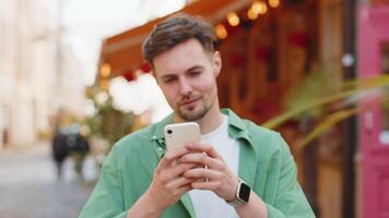 Man using smartphone typing text messages browsing internet, finishing work, looking at camera video