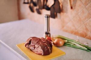 Piece of raw meat on a cutting board stands on a table in the kitchen next to spices and vegetables photo