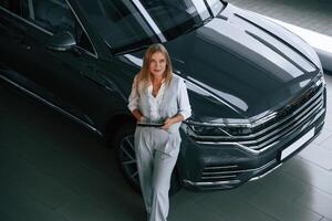 With tablet in hands. Woman in formal clothes is in the car dealership photo