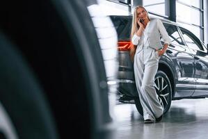 Talking by phone,. Woman in formal clothes is in the car dealership photo