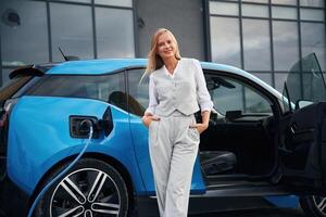Standing and ,posing. Woman ,on, the electric cars charge station at daytime photo
