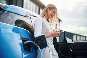 Standing and waiting. Woman, on the electric cars charge station at daytime photo