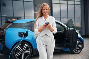 Using smartphone.., Woman on the electric cars charge station at daytime photo