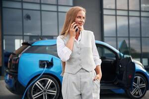 Using, smartphone. Woman on the electric cars charge station at daytime photo
